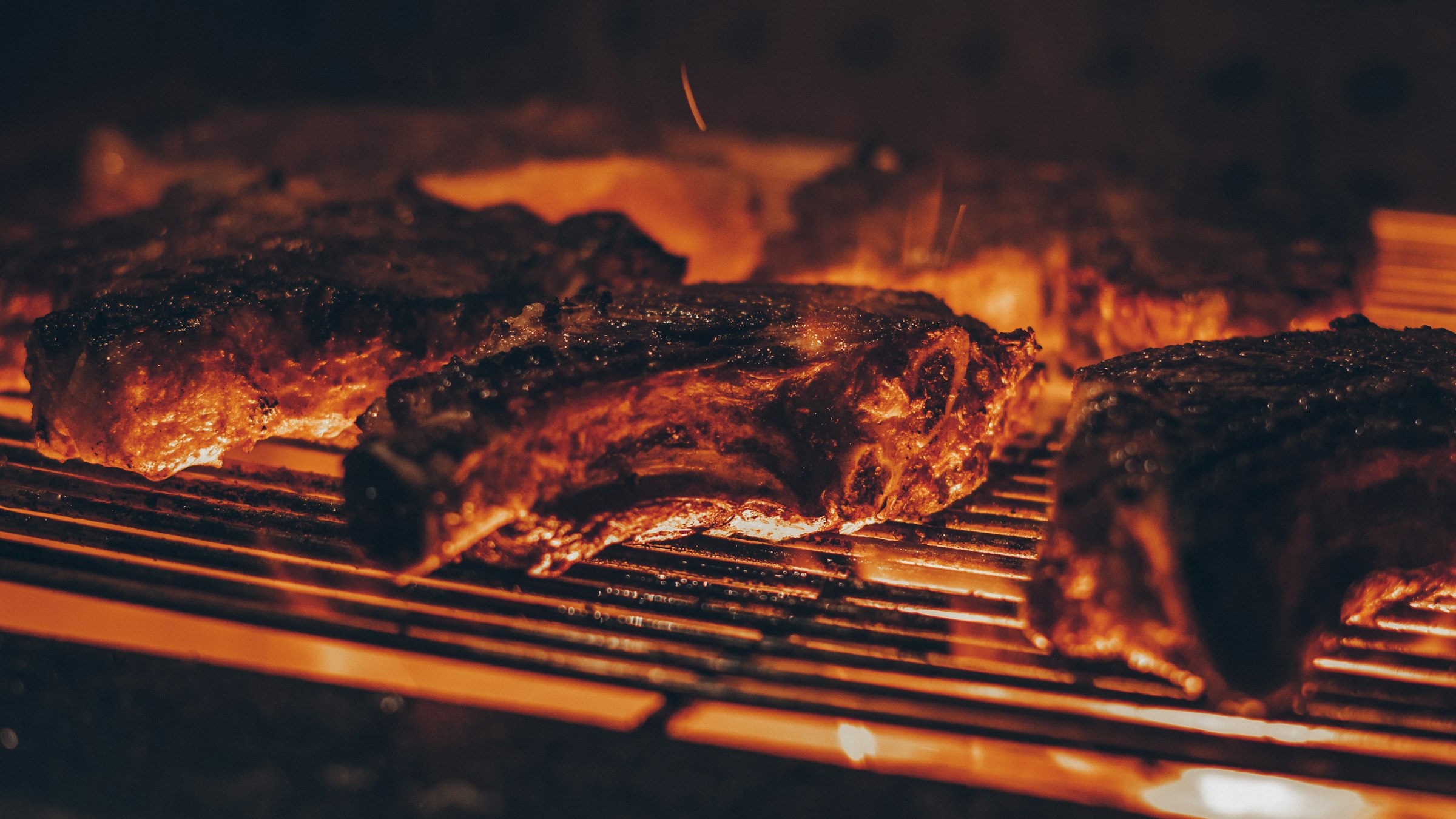 Carne selando sobre a brasa, com o fogo passando pela grelha